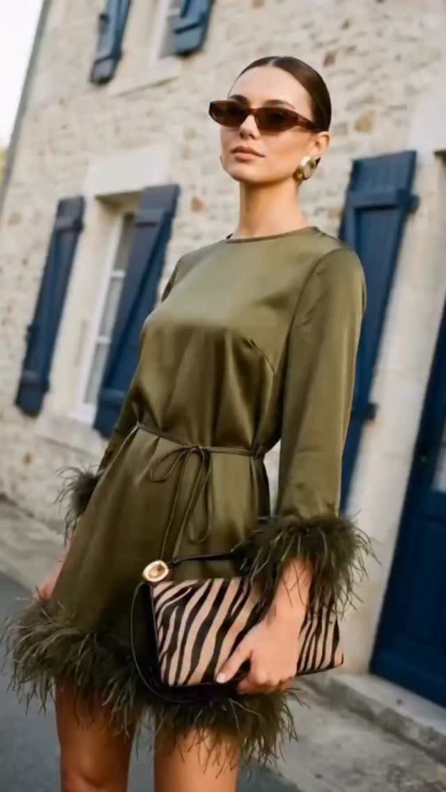 Woman in olive green satin mini dress with feather trim and zebra-print clutch.