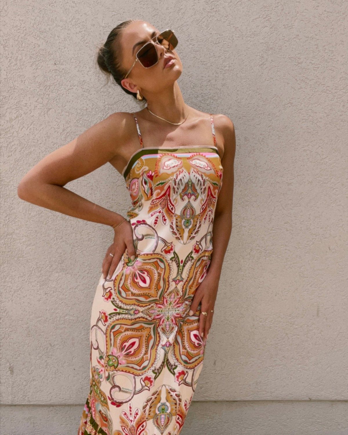 Woman in a long paisley print maxi dress posing against a neutral wall