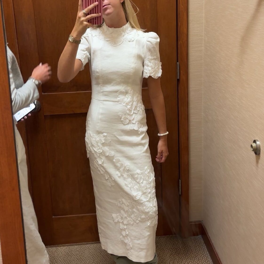 Woman in a white high-neck midi dress with floral lace applique details.
