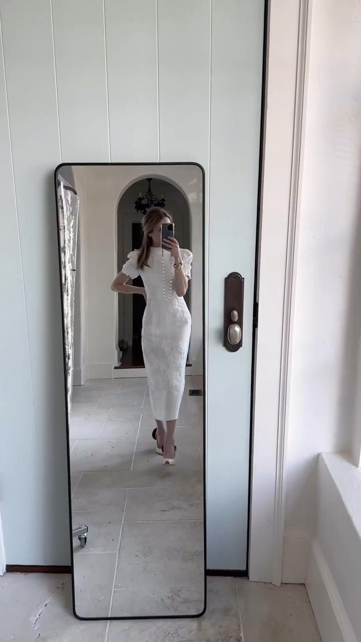 Woman in a white textured midi dress posing for a mirror selfie indoors.