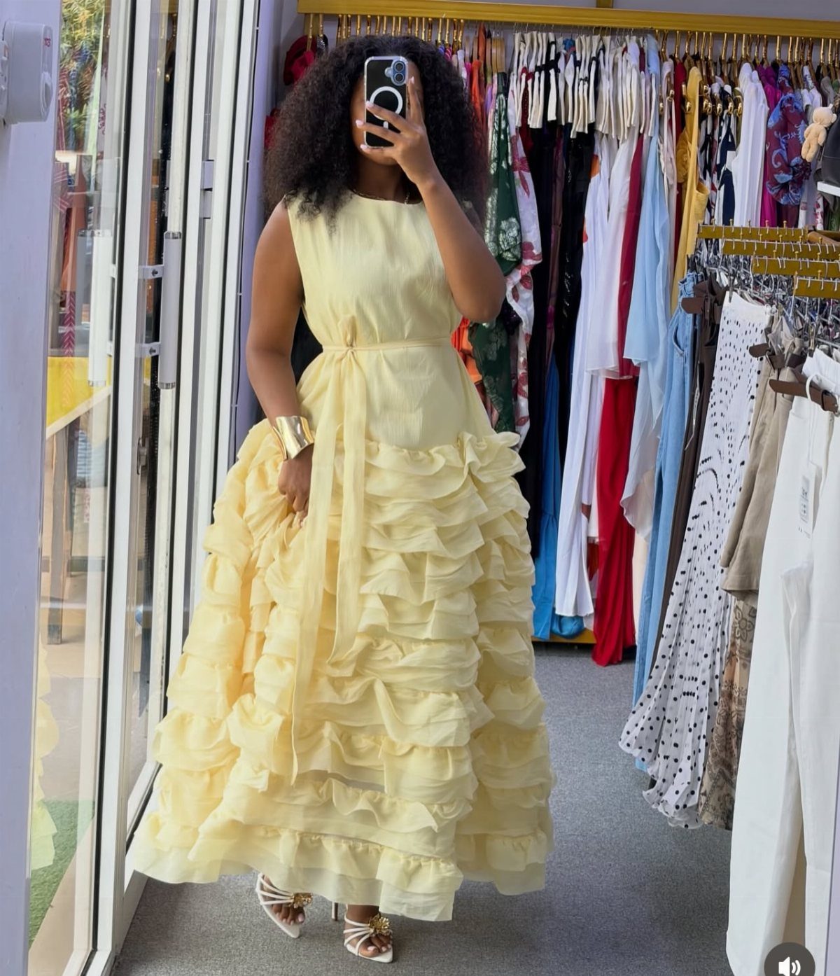 Woman wearing a pale yellow sleeveless gown with tiered ruffles in a clothing store