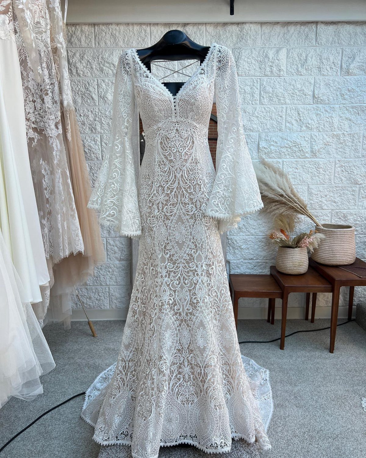Boho Wedding Dress Looks: 8 Ideas from Lace to Chiffon 2 White lace bohemian wedding dress with long bell sleeves hanging against a stone wall.