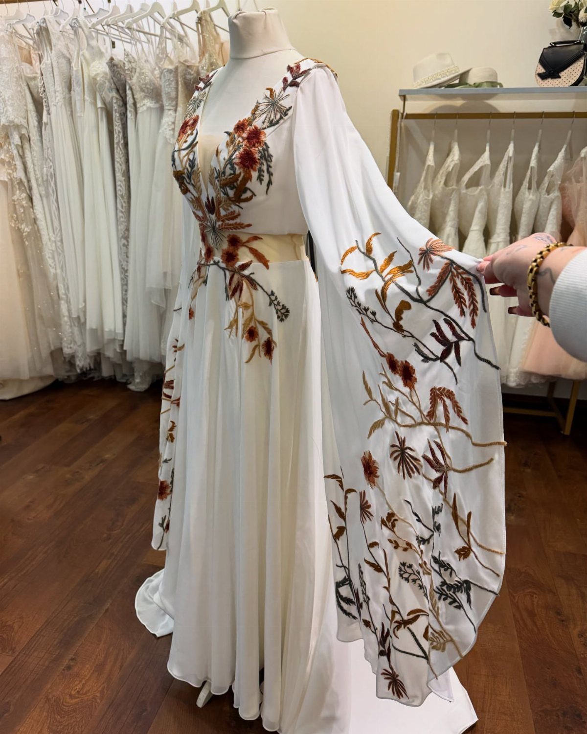 Boho Wedding Dress Looks: 8 Ideas from Lace to Chiffon 7 White boho wedding dress with floral embroidery and bell sleeves on a mannequin.