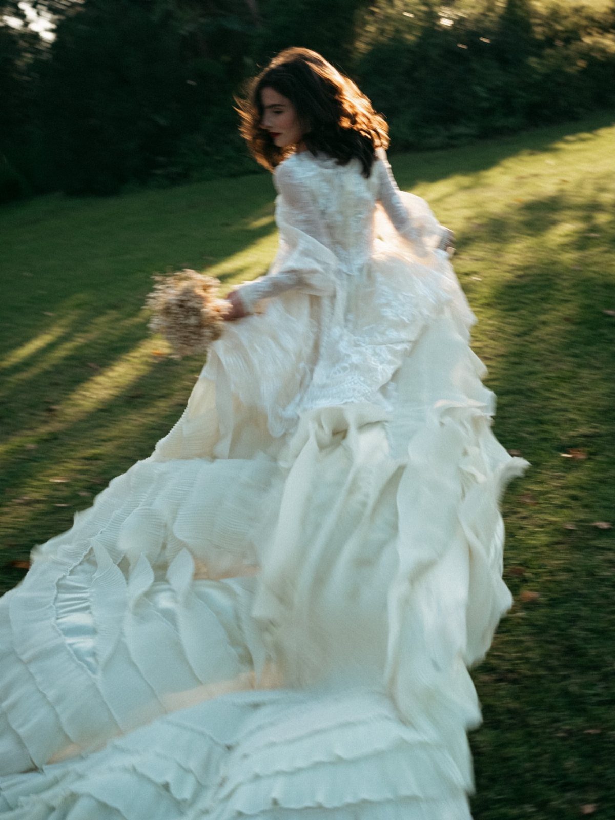 Boho Wedding Dress Looks: 8 Ideas from Lace to Chiffon 8 Woman in a ruffled white boho wedding dress walking through a green field.