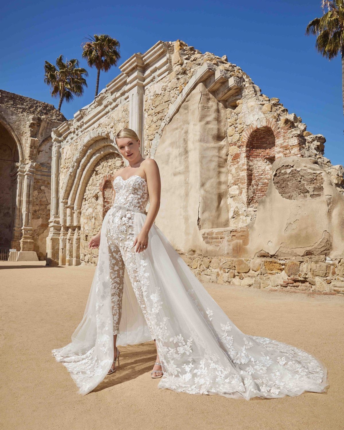 Bride Reception Dress: 17 Ideas for Your Second Look 12 Woman in a white lace bridal jumpsuit with a long train at stone ruins.