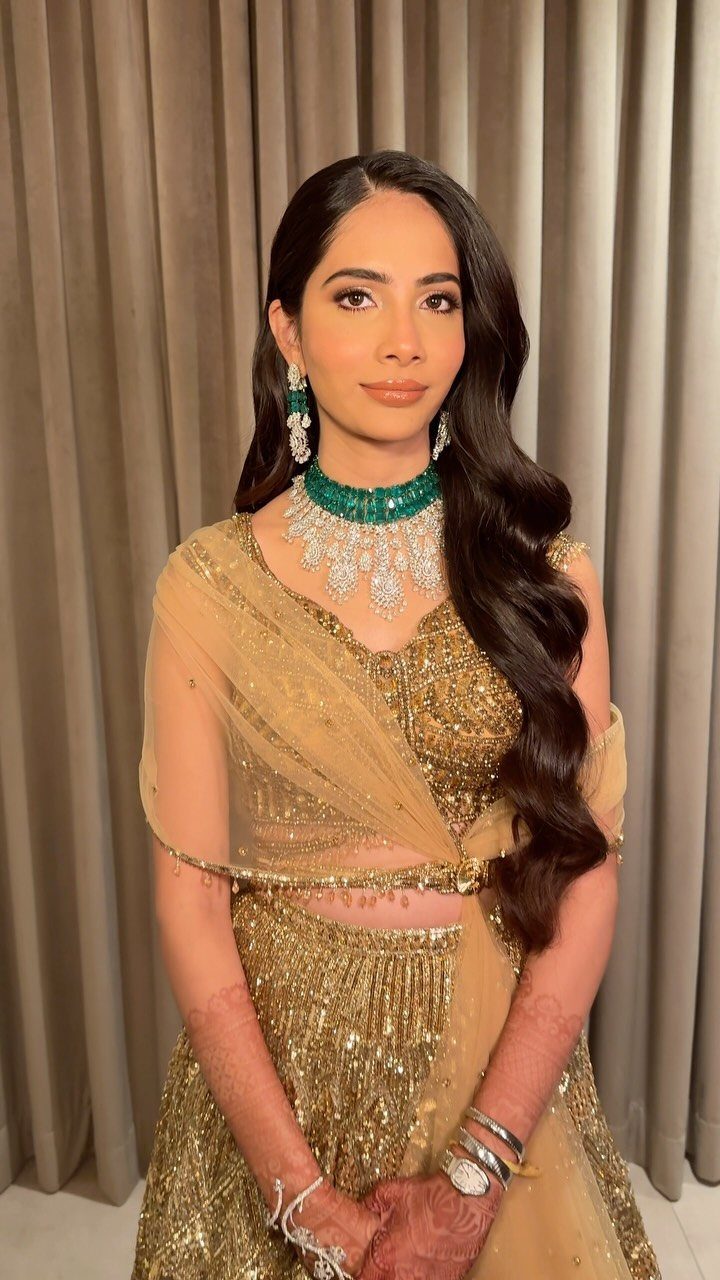 Bride Reception Dress: 17 Ideas for Your Second Look 9 Woman in a gold sequined bridal lehenga with emerald jewelry posing against curtains.