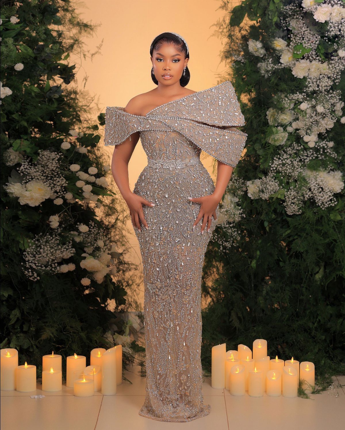 Bride Reception Dress: 17 Ideas for Your Second Look 15 Woman in a sparkling silver off-the-shoulder reception gown standing among white flowers and candles.
