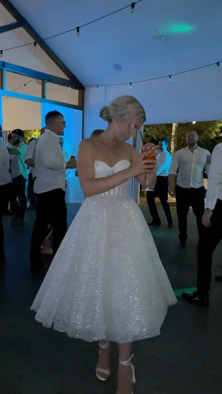 Bride Reception Dress: 17 Ideas for Your Second Look 1 Woman in a sparkly white strapless midi dress holding a drink at a party.