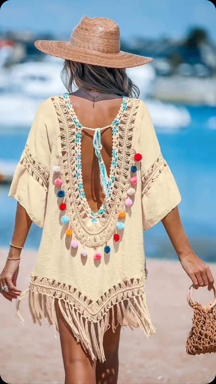Woman wearing a cream bohemian summer dress with pom-poms and a straw hat.
