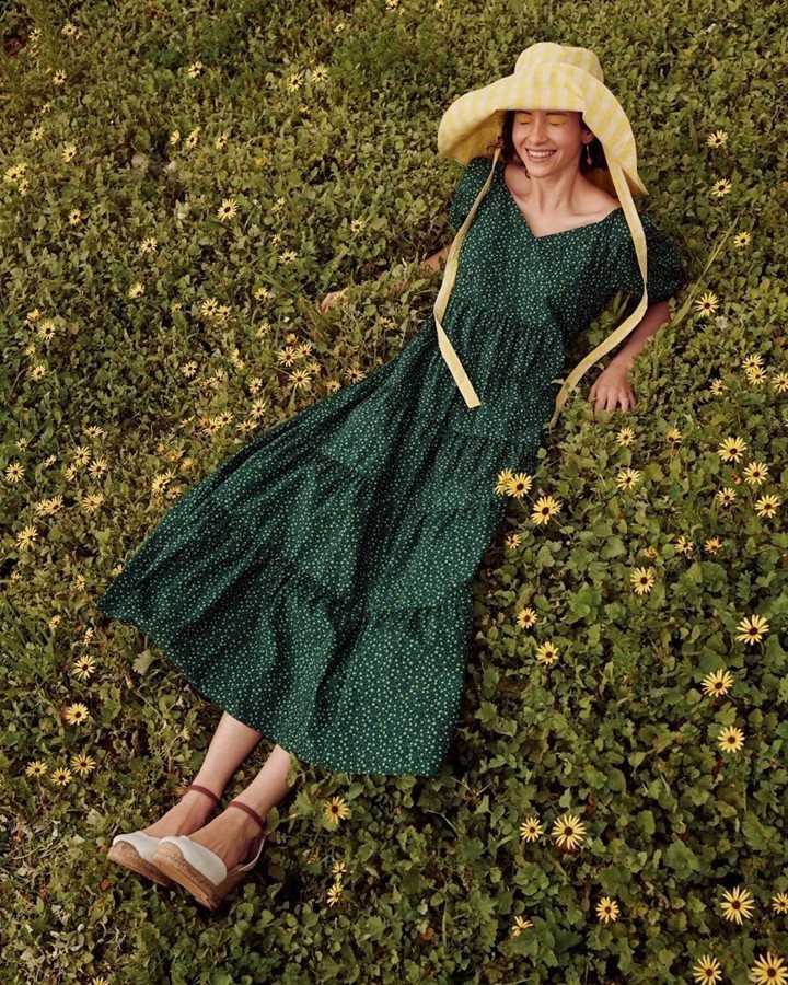 Woman in a green polka dot summer dress and yellow hat lying in grass.