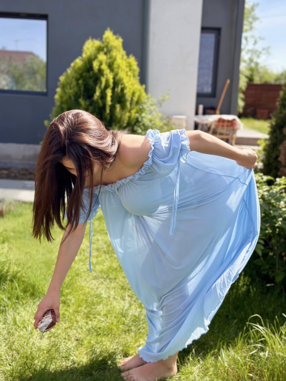 Woman in a light blue off-the-shoulder ruffle gauze dress leaning over in a garden.