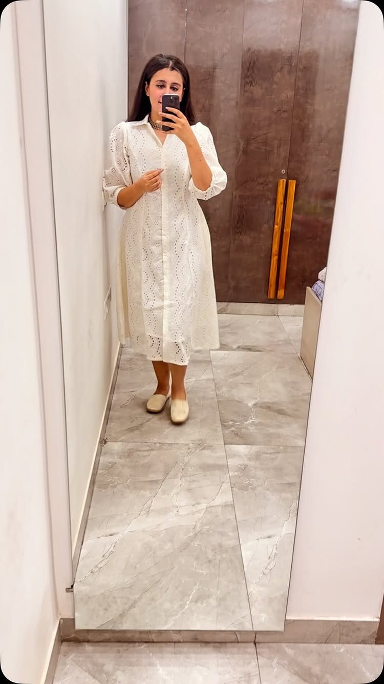 Woman in a white eyelet lace summer dress and beige flats taking a mirror selfie.