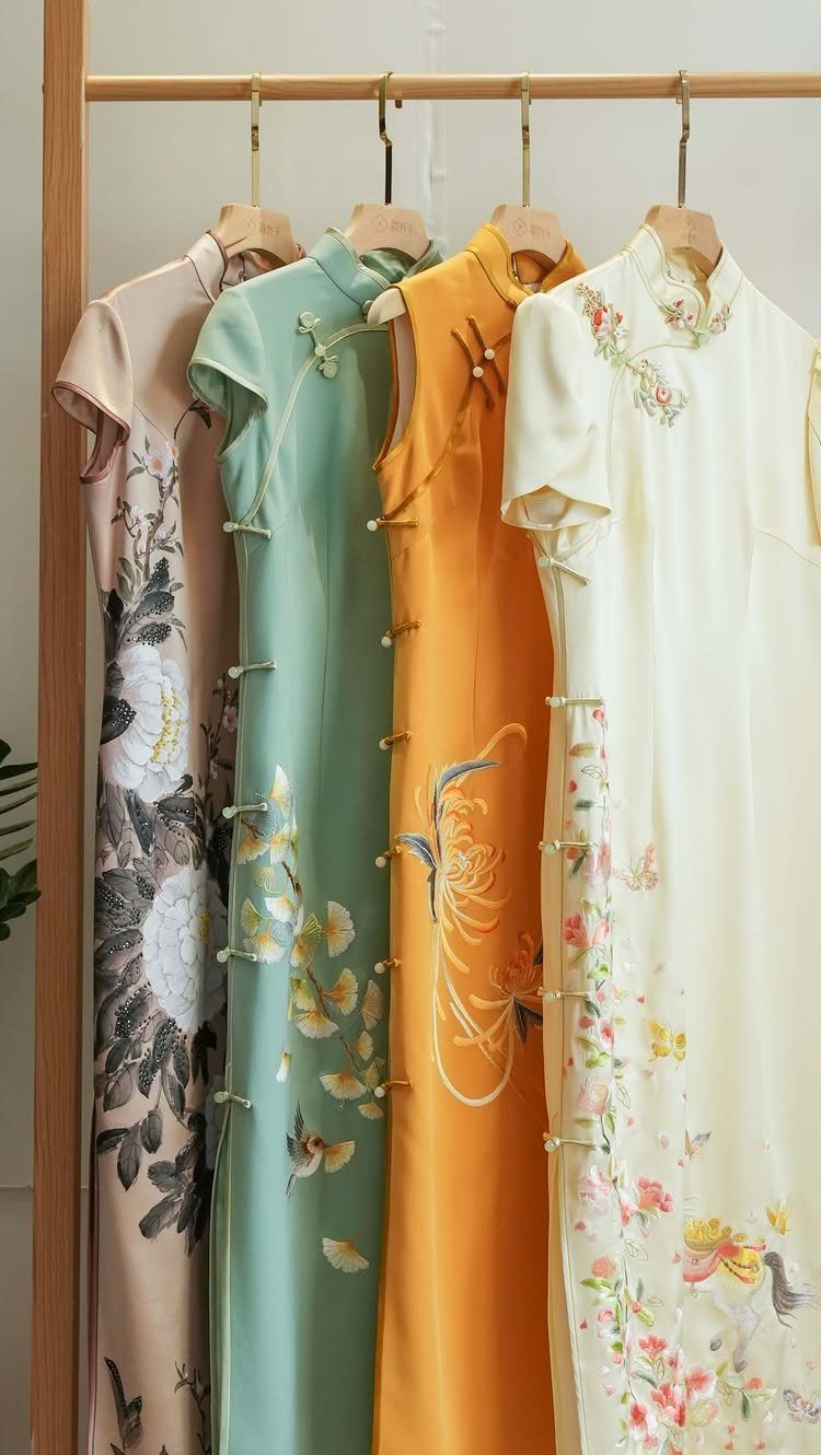 Four colorful qipao dresses with floral embroidery hanging on a wooden clothing rack.