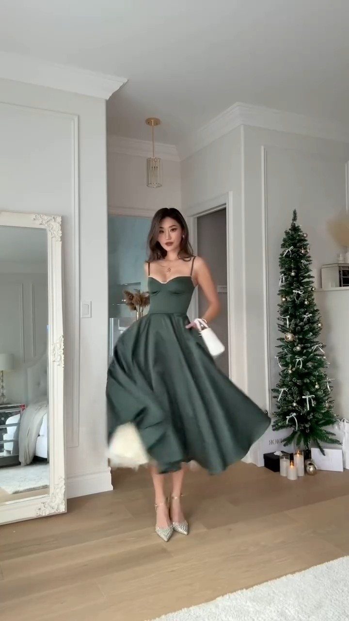 Woman in a dark green satin midi dress standing beside a Christmas tree.