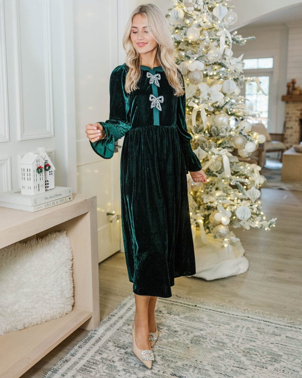 Woman in a long-sleeved dark green velvet dress standing by a Christmas tree.