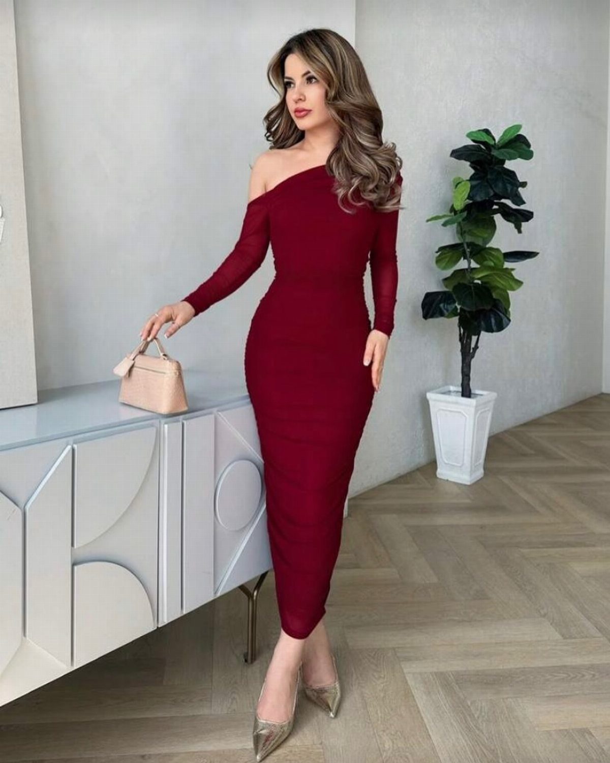 Woman in a burgundy off-the-shoulder long sleeve midi dress and gold heels.