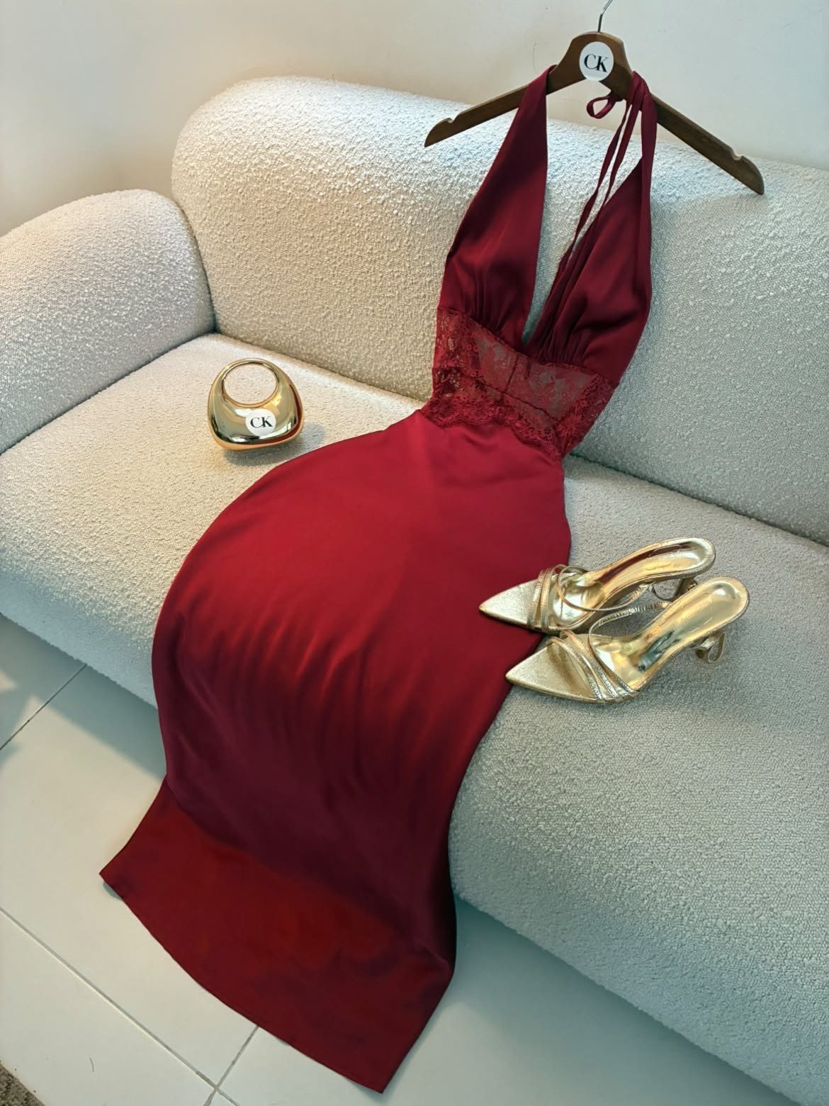 Red satin halterneck mini dress with gold heels and clutch on a white sofa