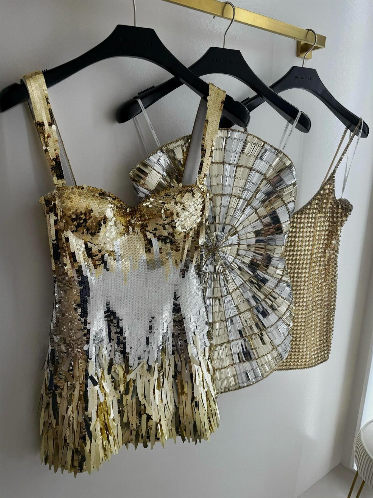 Three sparkly sequin mini dresses in gold and silver hanging on a clothing rack.