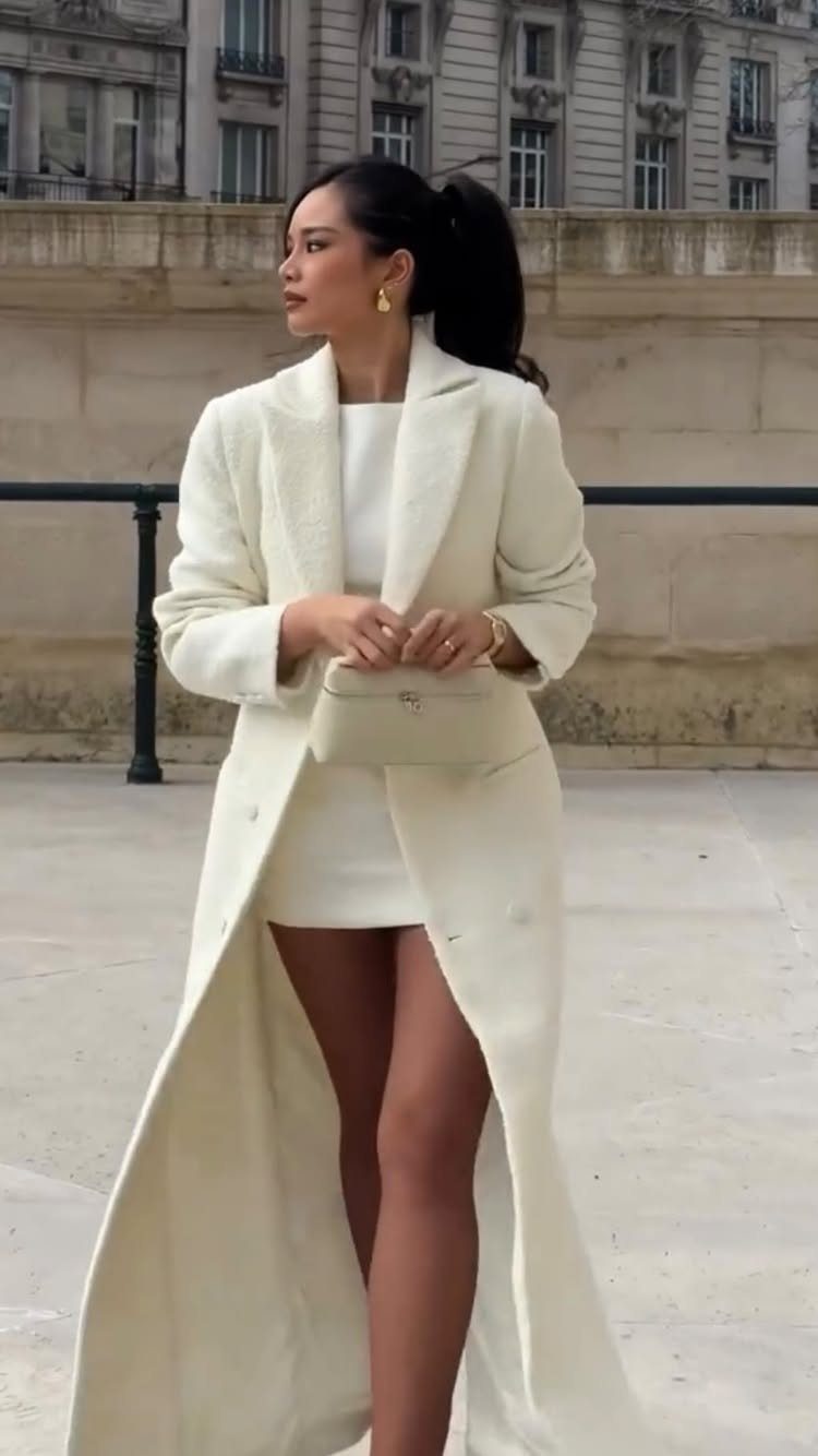 Classy Winter Dresses in 14 Timeless Styles 4 Woman in a white dress and long white coat posing before stone buildings.