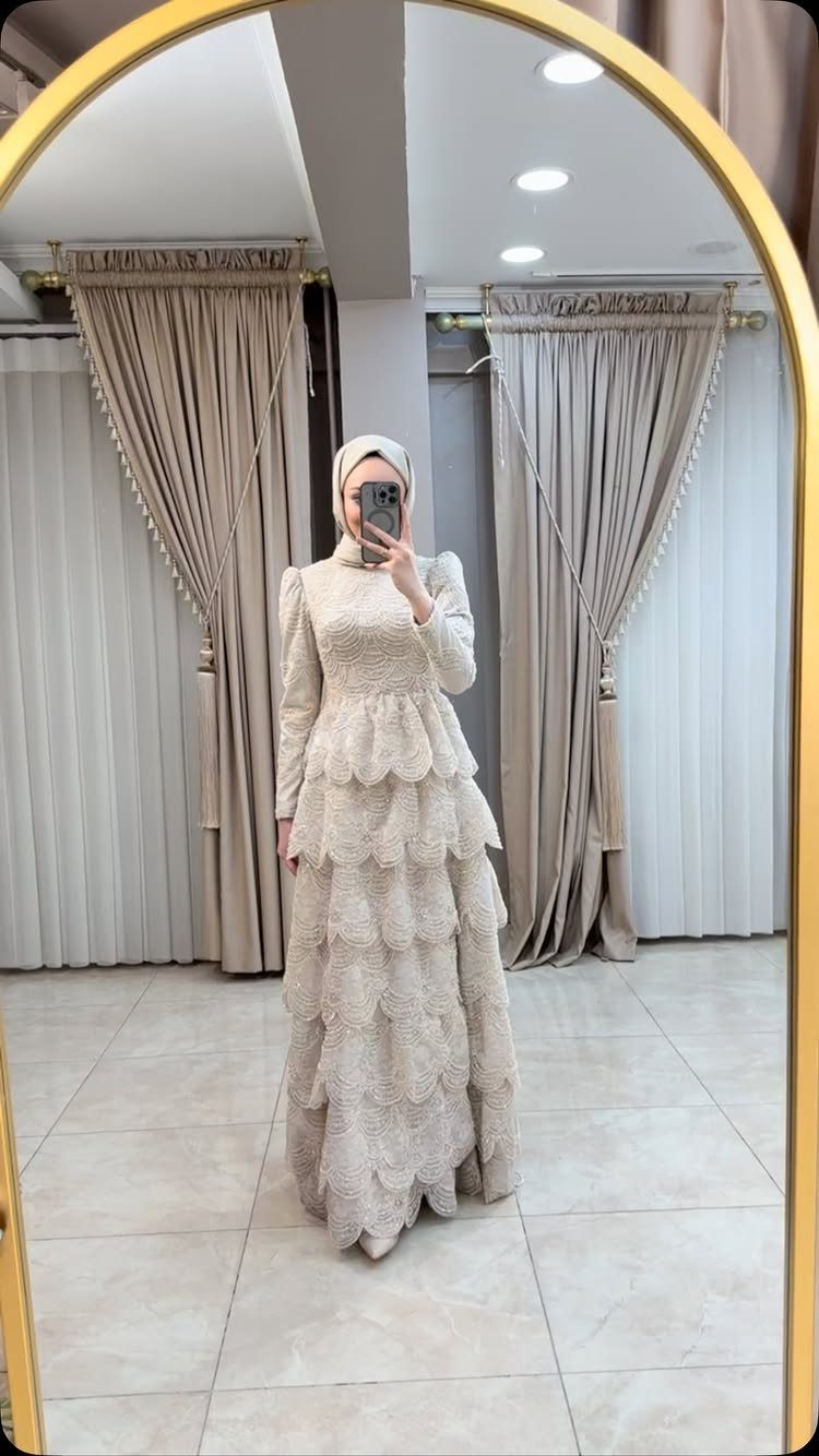 Classy Winter Dresses in 14 Timeless Styles 14 Woman in a white hijab and tiered lace winter dress taking a mirror selfie.