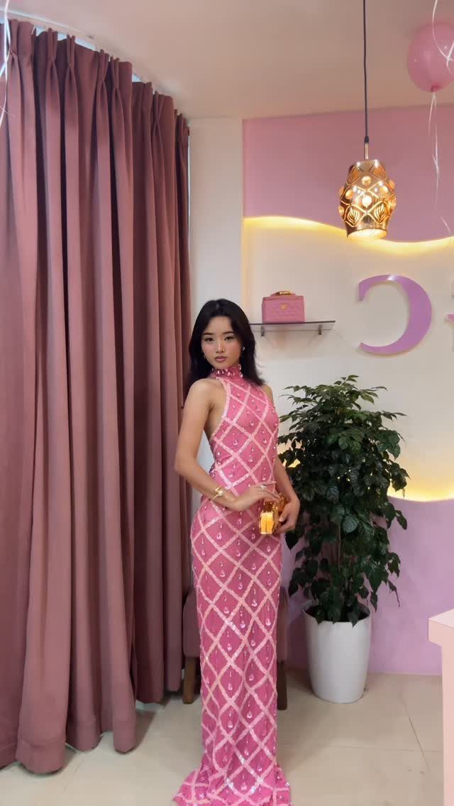 Woman in a long pink dress with sparkly white diamond patterns standing indoors.