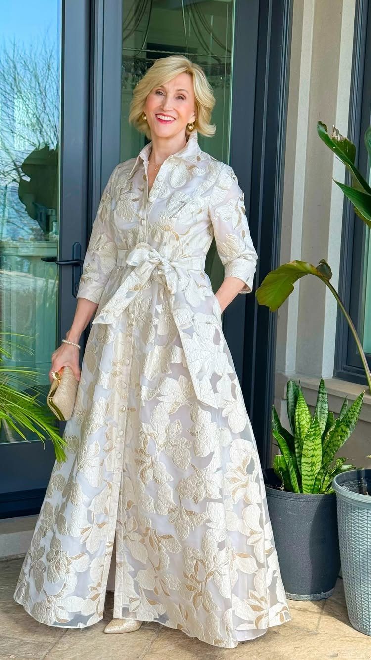 Blonde woman in an elegant cream floral maxi dress with a tied waist belt.