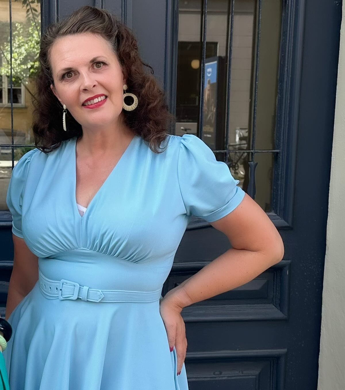 Woman wearing a light blue vintage-style dress with a belt and puffed sleeves.