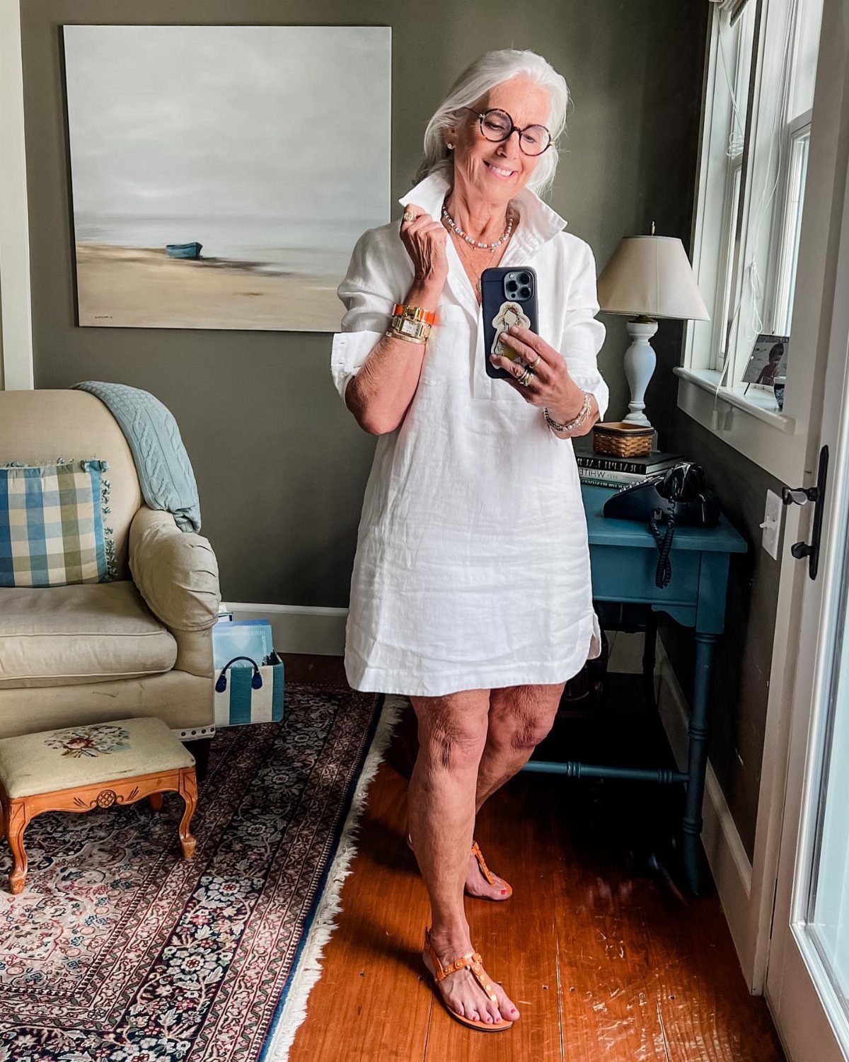 Older woman with white hair wearing a short white linen dress and sandals.