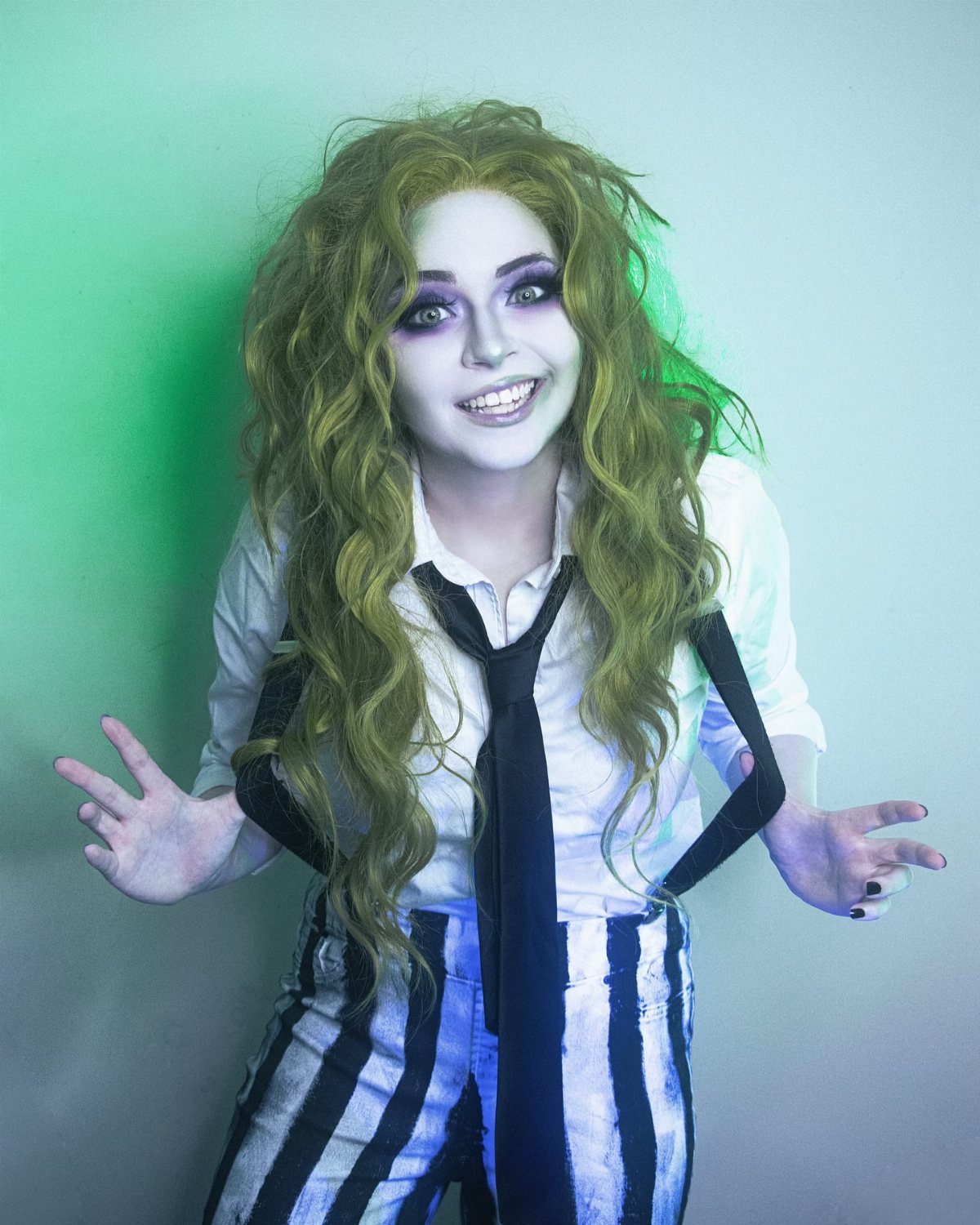 Person in Beetlejuice costume with pale makeup, green hair, and striped pants.