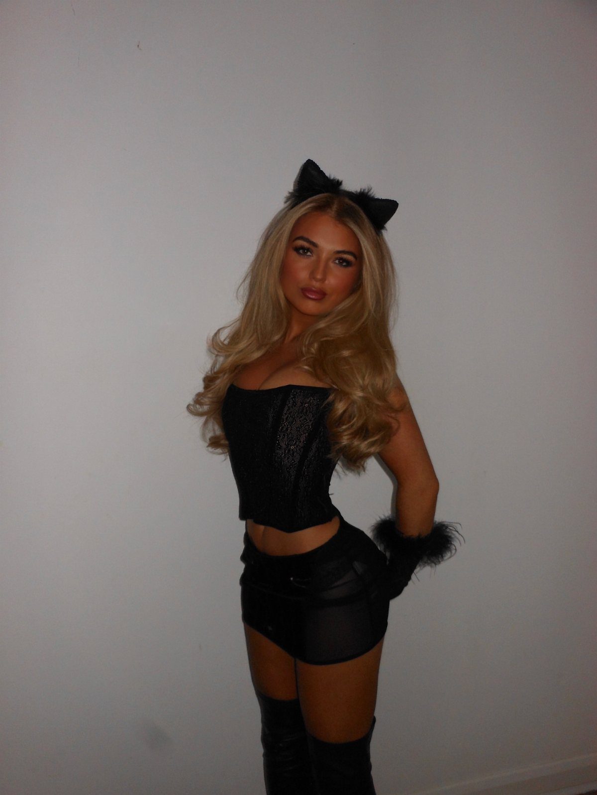 Woman wearing a black cat costume with cat ears, corset, and mini skirt.