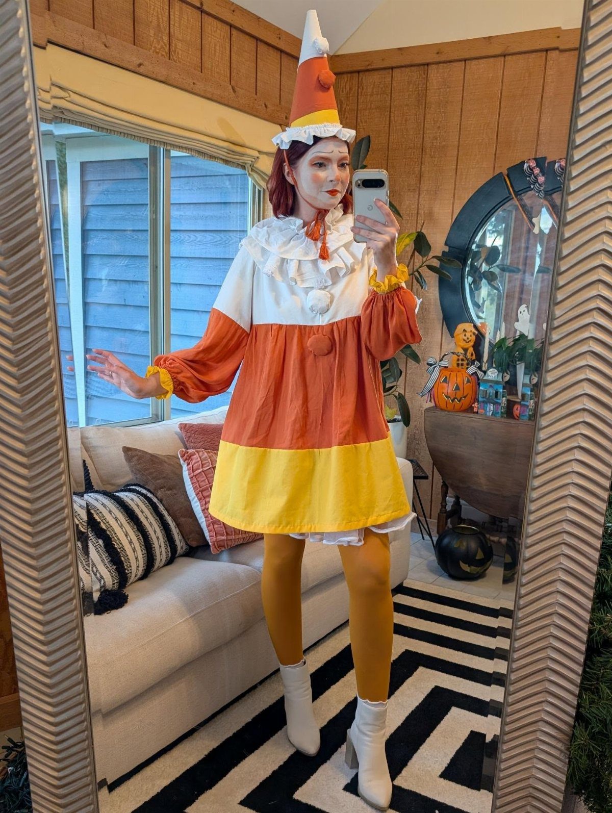 Person in a candy corn costume with a pointed hat posing in a mirror.