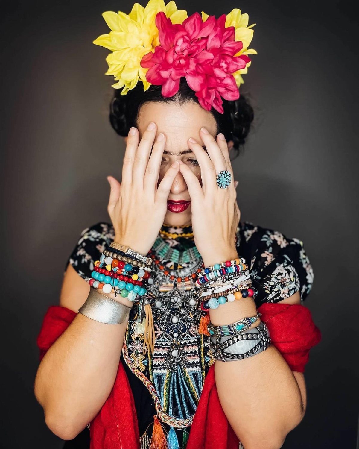 Woman dressed as Frida Kahlo with floral crown, colorful jewelry, and red shawl.