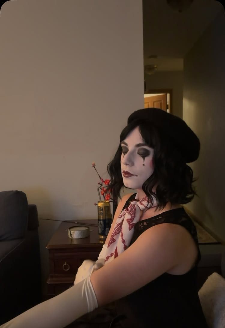 Woman dressed as a mime with white face paint, black beret, and gloves.