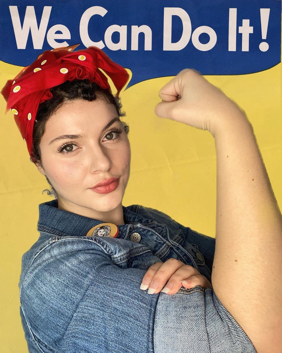 Woman in Rosie the Riveter costume with red headscarf and denim shirt flexing arm.