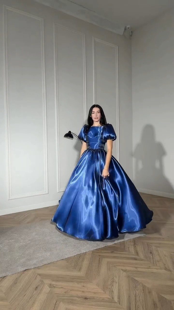 Woman wearing a voluminous royal blue satin ball gown with puffed sleeves in a room.