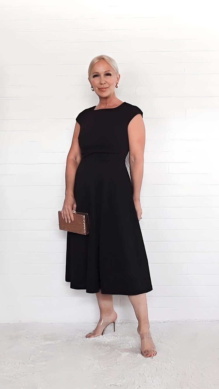 Elegant Dresses for Wedding Guests Over 50 (8 Refined Styles) 6 Mature woman wearing an elegant sleeveless black midi dress and nude heels.