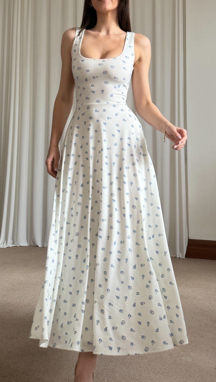 Woman wearing a white floral print maxi dress standing before white curtains