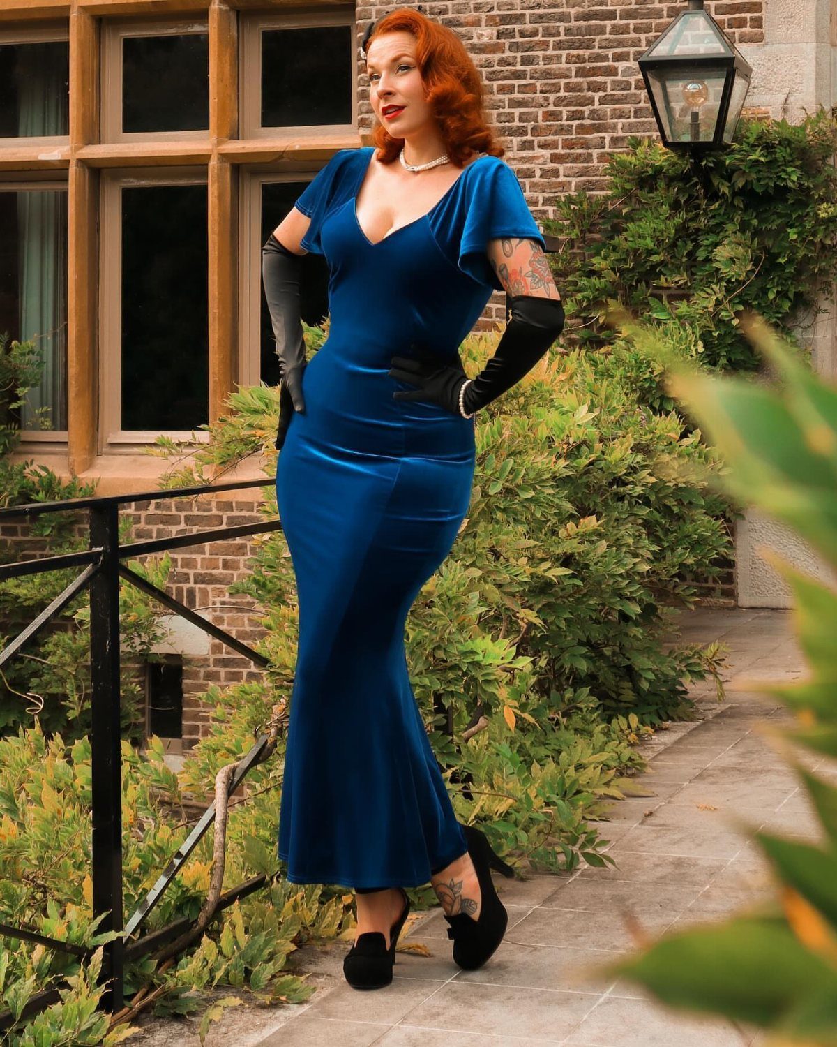 Woman in a royal blue satin maxi dress and black opera gloves outdoors.