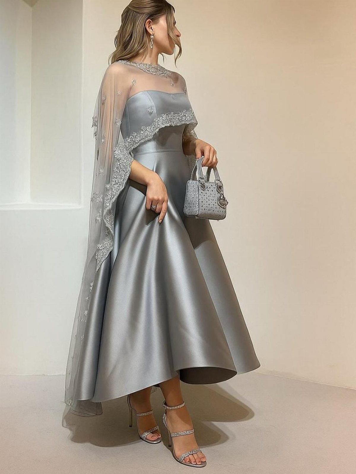 Woman in a silver satin midi evening gown with a sheer embroidered cape.