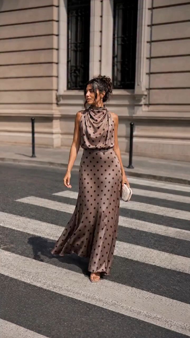 Woman in a taupe polka dot satin gown walking across a city street crosswalk.