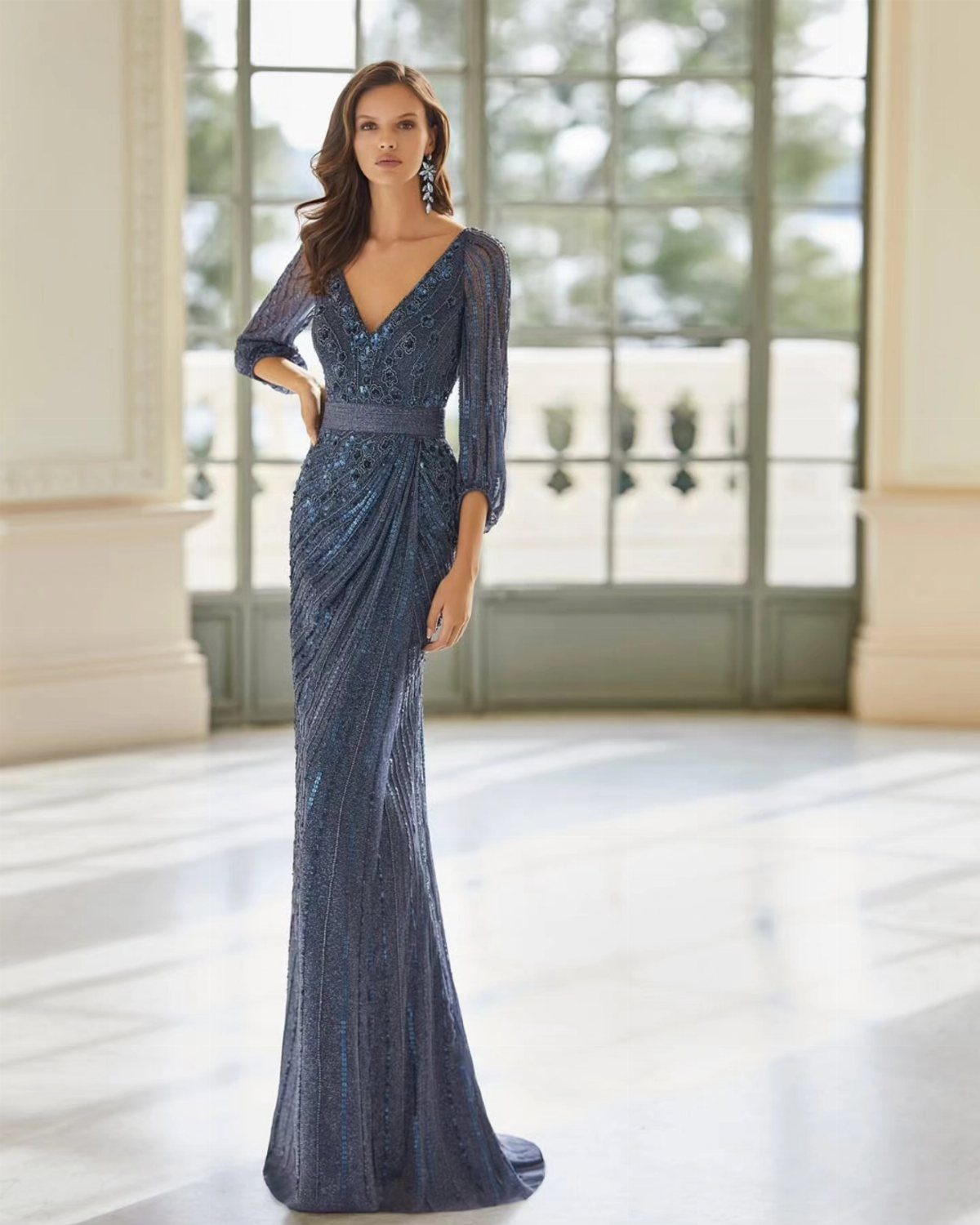 Woman in a sparkling navy blue V-neck evening gown standing in a bright room