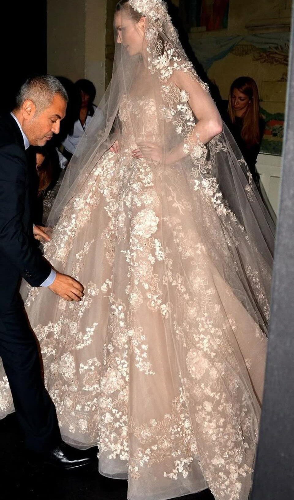 Woman in a voluminous champagne floral lace bridal gown with a long sheer veil.