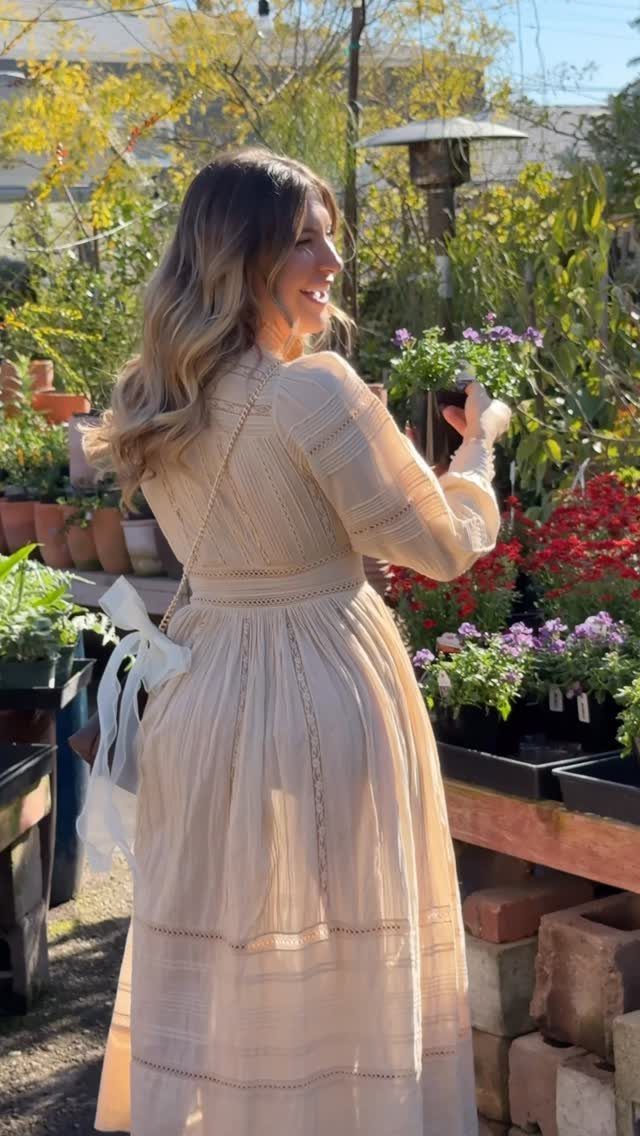 Woman in a cream tiered maxi dress browsing flowers at a plant nursery