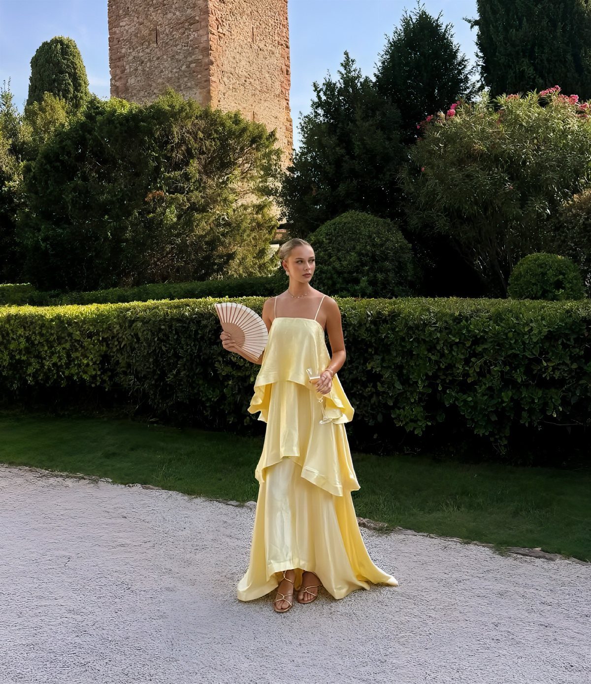 Woman in a tiered yellow satin dress holding a fan in a garden