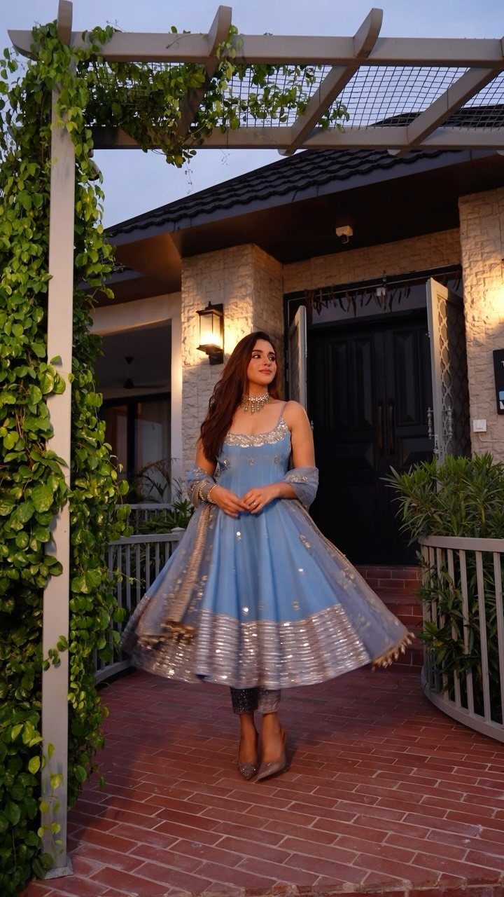 Woman in a light blue Anarkali suit with silver embroidery on a brick patio.