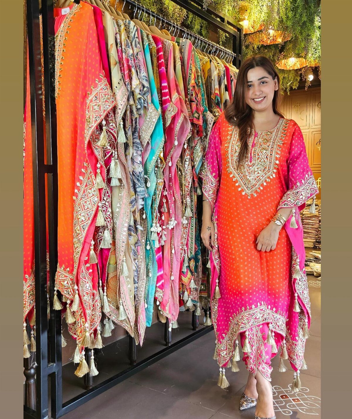 Woman wearing a bright orange and pink embroidered kaftan dress in a boutique.