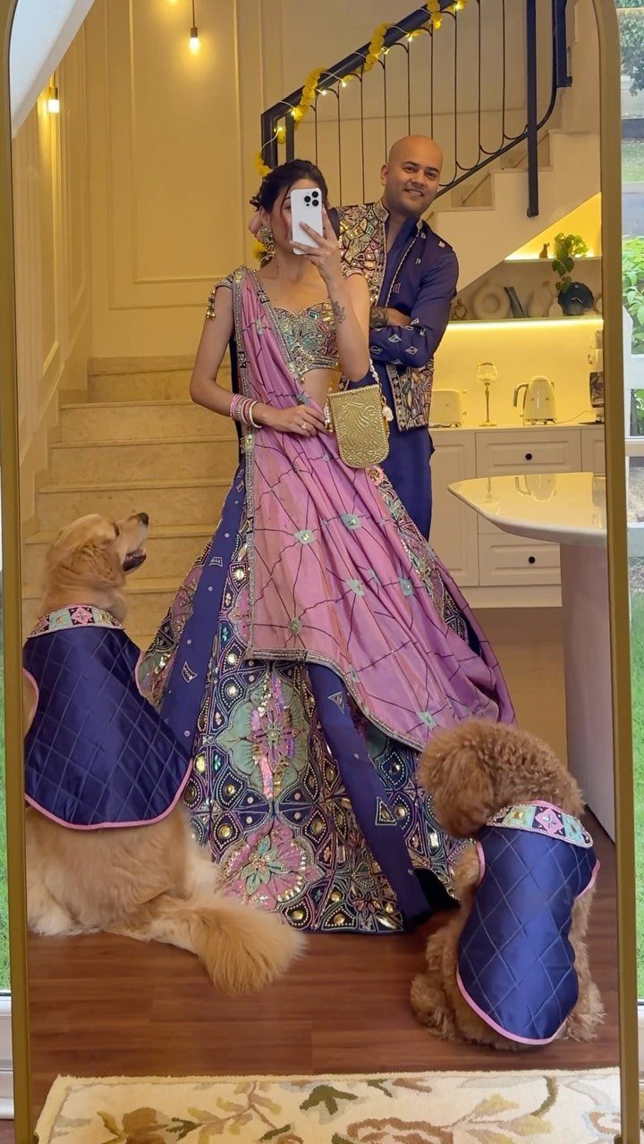 Woman wearing a purple and pink embroidered lehenga choli posing with a man and dogs.