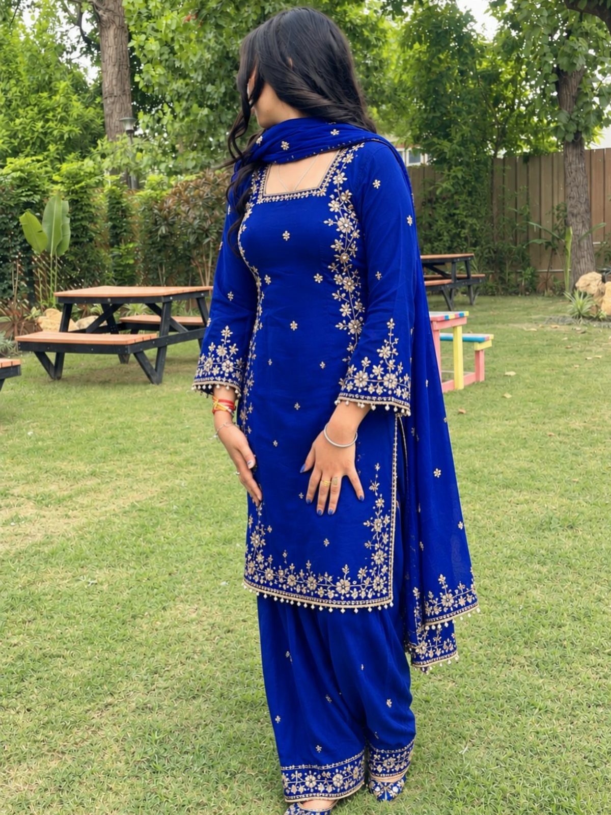Woman in royal blue Patiala suit with gold embroidery standing on green grass