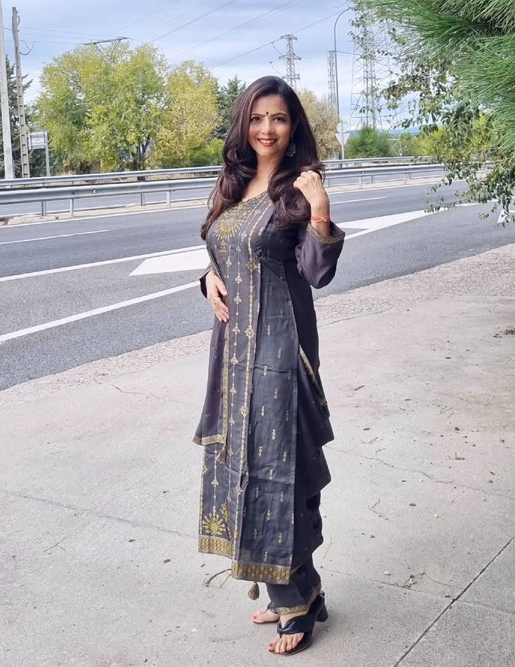 Woman wearing a dark grey Salwar Kameez with gold embroidery standing on a sidewalk.