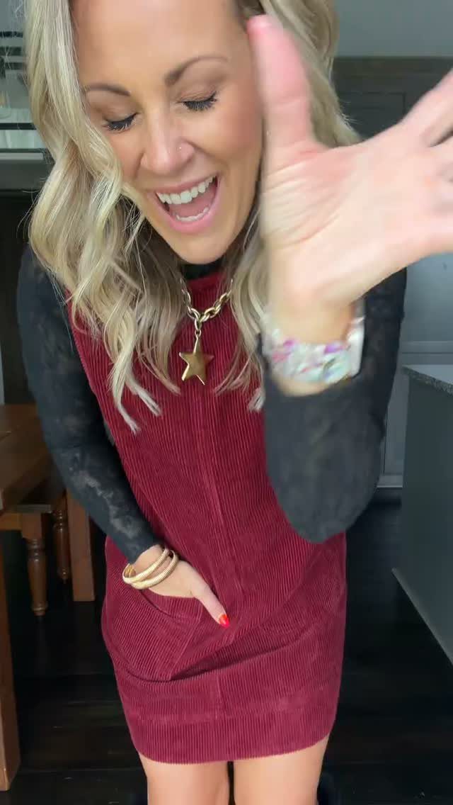 Woman wearing a maroon corduroy jumper dress over a black long-sleeved shirt.